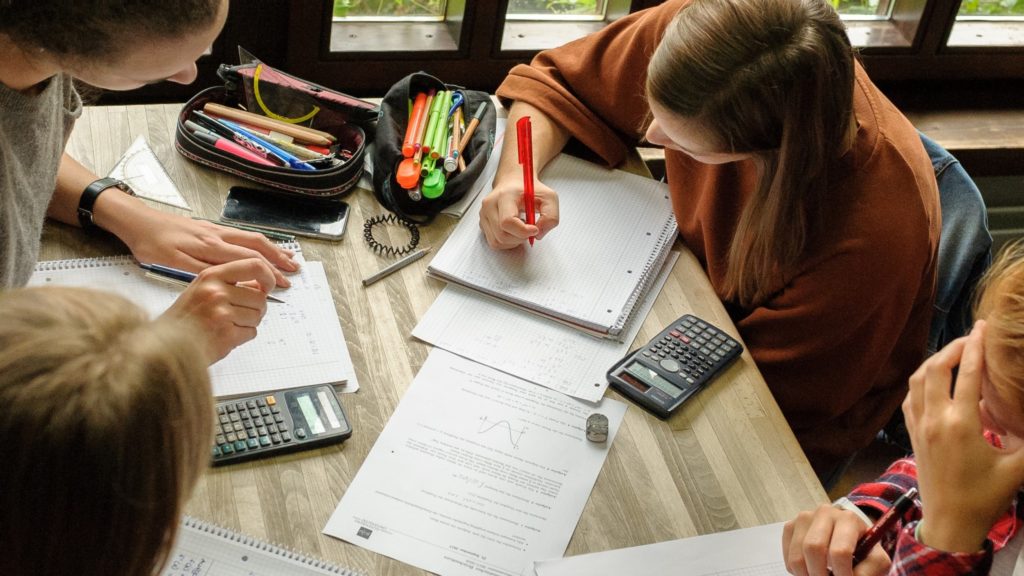 Studierende sitzen an einem Tisch und arbeiten gemeinsam an Mathe-Aufgaben.